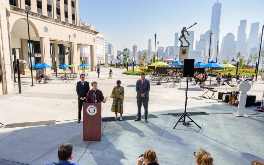 Exchange Place Alliance Director of Development and Operations Martin Schmid stands at the podium at the newly renovated pedestrian plaza, with the New York City skyline in the background. - EXCHANGE PLACE ALLIANCE