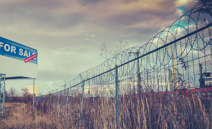 Abandoned property/brownfield site with For Sale sign and barbed wire.